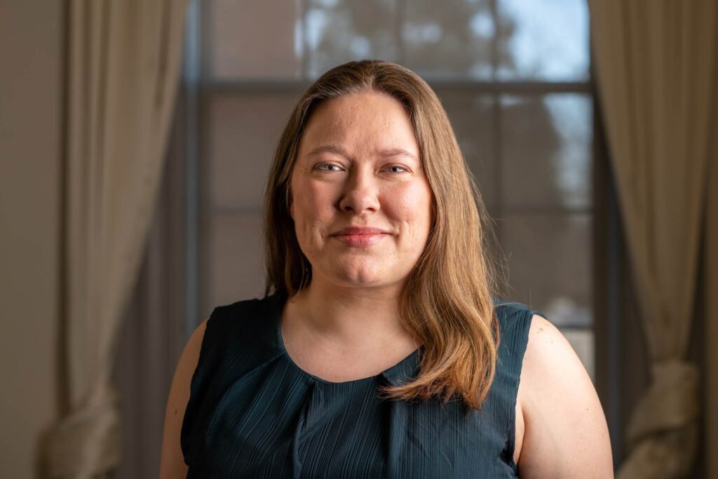 Cera is a white woman with light brown hair. She is wearing a teal top and is smiling at the camera.