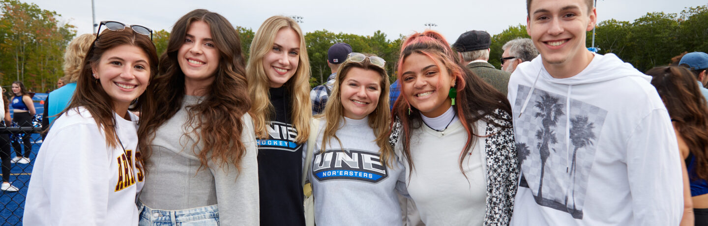 A group of students smile and pose together at a U N E football game