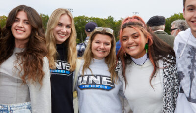 A group of students smile and pose together at a U N E football game