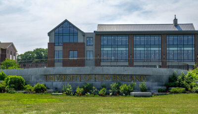 A long brick building sits behind a stone sign that reads 