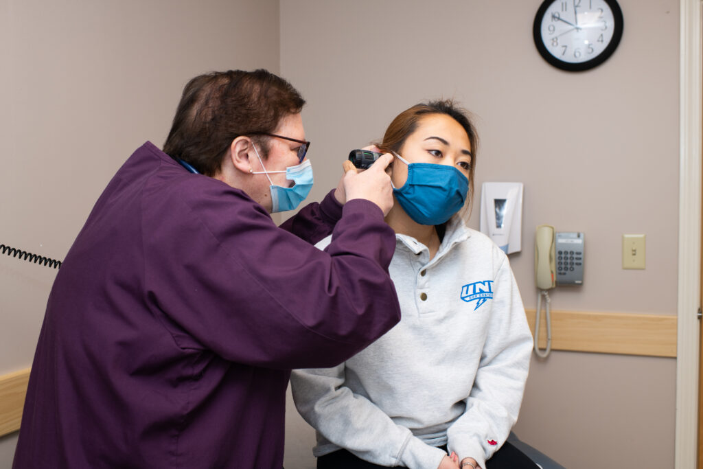 A U N E student health services nurse looks in the ear of a student patient