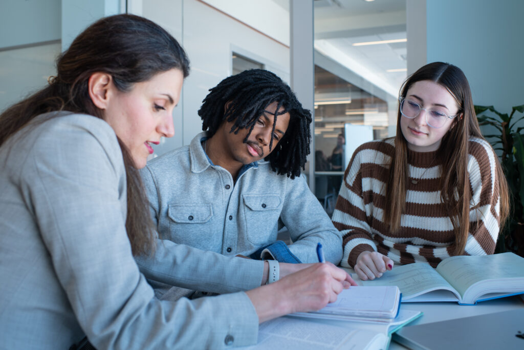 A professor assists two U N E students with their notes