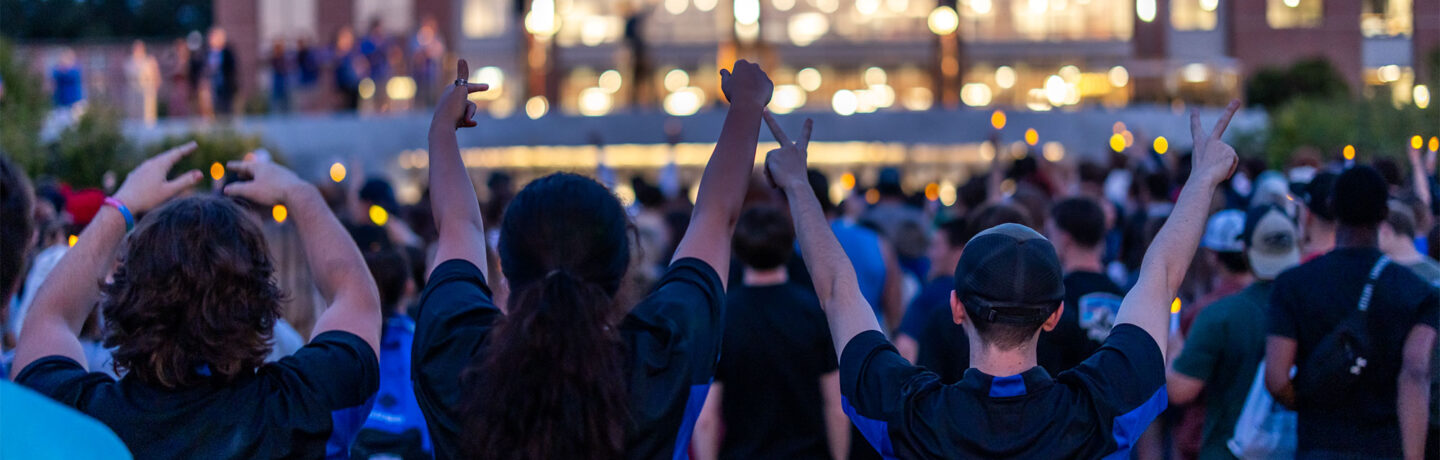 Students cheering in front of a light-up building at night