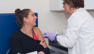 A U N E healthcare professional gives a student a vaccine via a shot in their upper arm