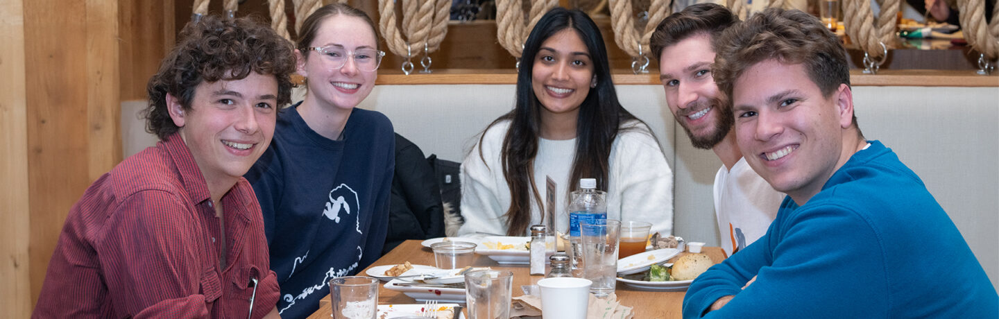 A group of students smiling for the camera from their booth in the dining hall
