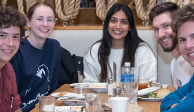 A group of students smiling for the camera from their booth in the dining hall