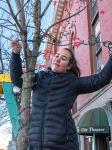 Student volunteer hangs decorative ribbons on tree branches during UNE's Give Back and Get Lit community service event in downtown Biddeford.