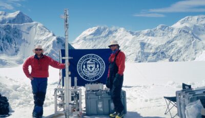 Dr. Wake and Dr. Kreutz standing at an ice core drilling site in front of a snow covered mountain